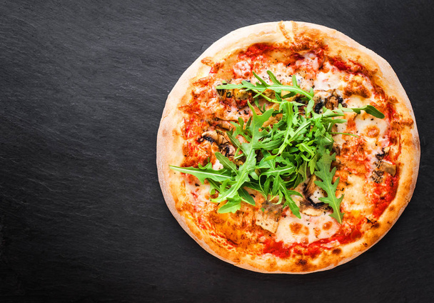 Pizza with tomatoes, mozzarella cheese and arugula. Pizza menu.Top view with copy space on dark stone table - Photo, Image
