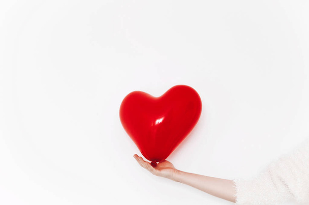 female hand in white sweater holding red balloon heart isolated  white background with copy space - Photo, Image