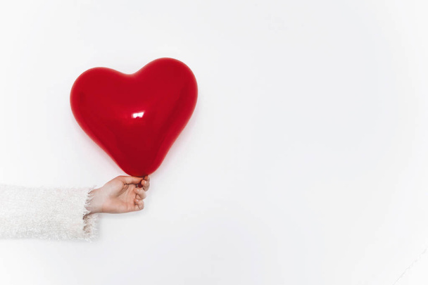 female hand in white sweater holding red balloon heart isolated  white background with copy space - Foto, Imagem