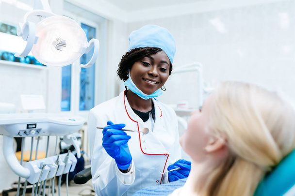 Odontóloga afroamericana atendiendo a paciente en clínica. Concepto de clínica dental
. - Foto, Imagen