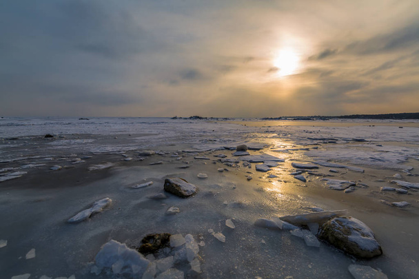 Piedras, témpanos de hielo y un mar helado en los rayos del sol al atardecer. Paisaje invierno
 - Foto, Imagen