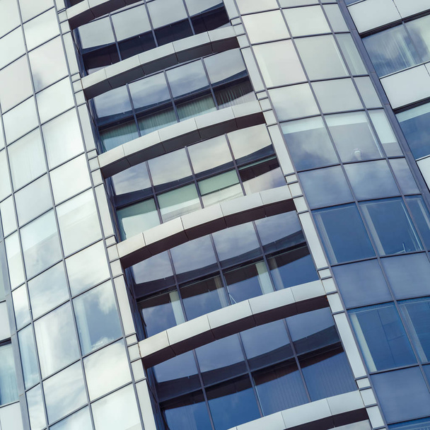 Parte de la fachada de un edificio moderno de gran altura y el reflejo de las nubes en sus ventanas
 - Foto, imagen