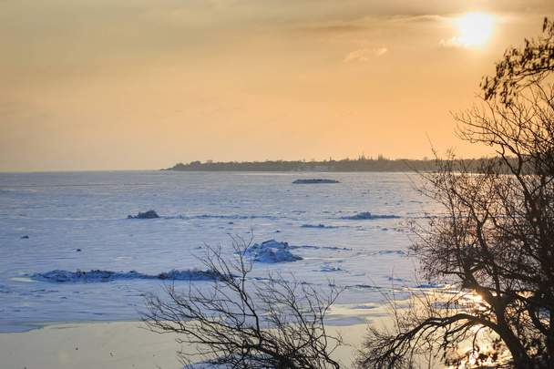 Costa del mar congelado en invierno, hummocas de hielo, reflejo en el agua de los rayos del sol al atardecer
 - Foto, Imagen
