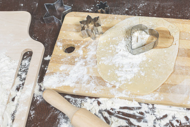 La masa se encuentra en un tablero de madera junto con los cortadores de galletas de diferentes formas
 - Foto, Imagen