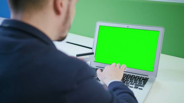 A Young Man Using a Laptop with a Green Screen - Foto, afbeelding