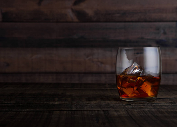 Glass of whiskey with ice cubes on wooden table - Foto, afbeelding