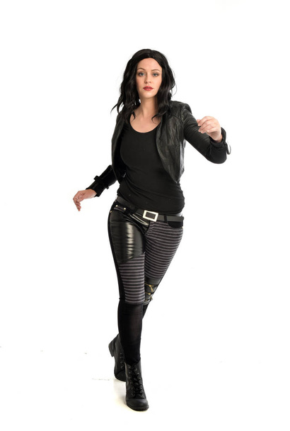 full length portrait of black haired girl wearing leather outfit. standing pose on a white background. - Photo, image