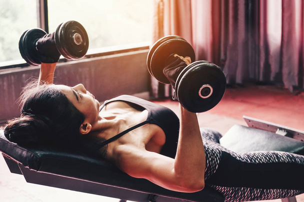 Asian sports woman doing exercises with dumbbell weights in gym - Foto, imagen