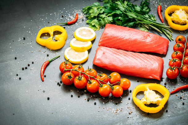 rohes Thunfischfiletfleisch auf Holzschneidebrett mit Gemüse und Zutaten zum Kochen auf schwarzem Steinhintergrund - Foto, Bild