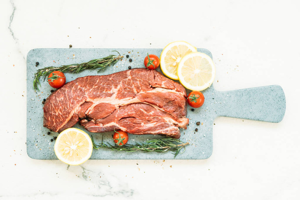 Viande de bœuf crue sur planche à découper avec légumes et ingrédients pour la cuisson
 - Photo, image