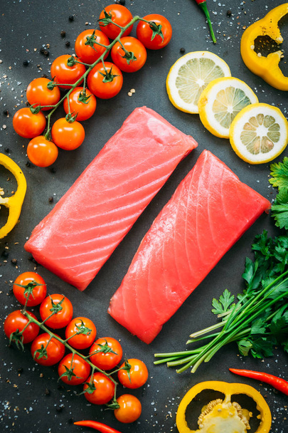 Surowy tuńczyk filet mięsa na deska do krojenia z warzyw i składniki do gotowania na czarnym tle kamień - Zdjęcie, obraz