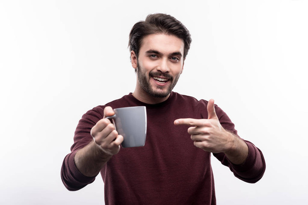 Cheerful young man pointing at the cup of coffee - Zdjęcie, obraz
