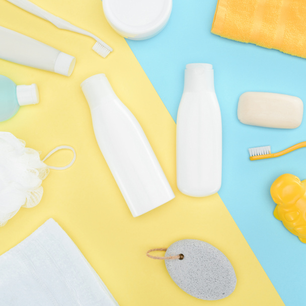 flat lay with body lotion in bottles, toothbrushes, pumice, towel and soap, isolated on blue and yellow - Photo, Image