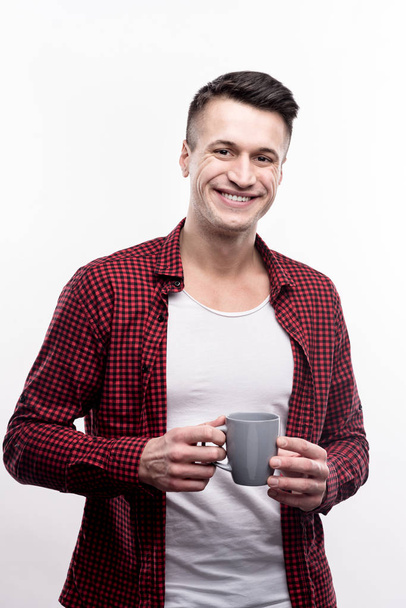 Cheerful young man in checked shirt holding cup of coffee - Photo, image
