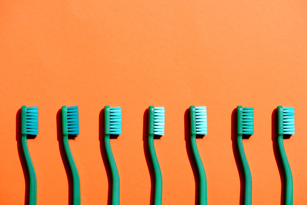 green toothbrushes in row, on orange with copy space - Fotografie, Obrázek