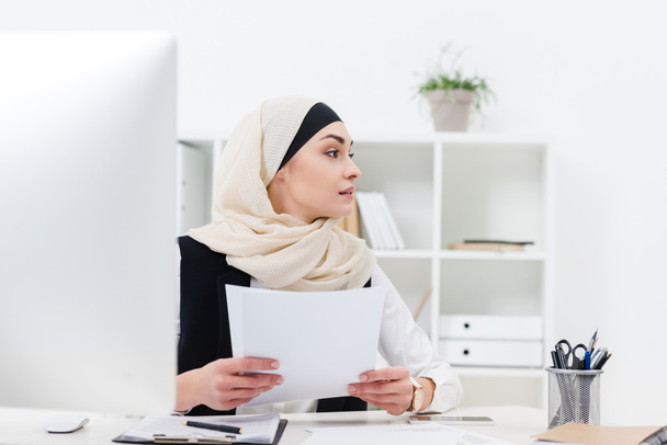 arabic businesswoman with papers in hands looking away at workplace - Photo, image