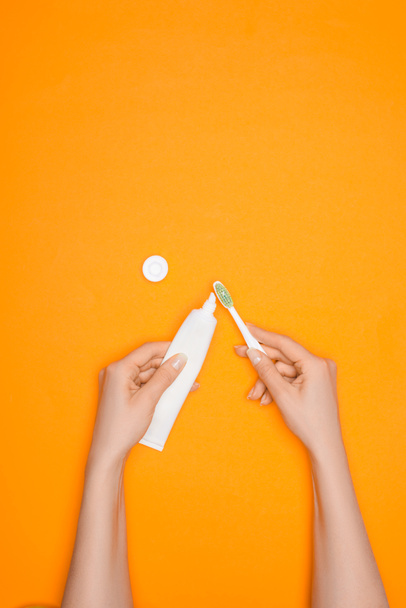 cropped view of woman with toothbrush and tube of toothpaste, isolated on orange - Foto, Imagen