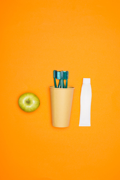 vista dall'alto di mela, spazzolini da denti in bicchiere di carta e tubo di dentifricio, isolato su arancione
 - Foto, immagini