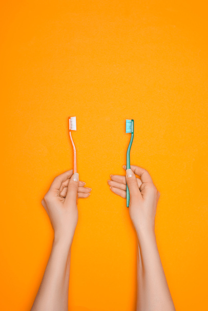bijgesneden beeld van vrouw met twee tandenborstels, geïsoleerd op oranje - Foto, afbeelding