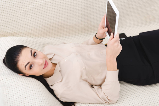 Glimlachende zakenvrouw met digitale tablet liggend op de Bank in kantoor - Foto, afbeelding