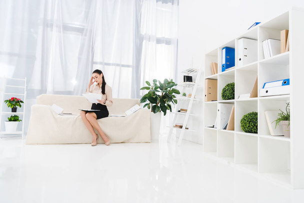 overworked businesswoman doing paperwork while sitting on sofa in office - Photo, Image
