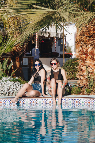 schöne junge Frauen mit Sonnenbrille lächeln in die Kamera, während sie sich in der Nähe des Swimmingpools im Resort in Ägypten ausruhen  - Foto, Bild