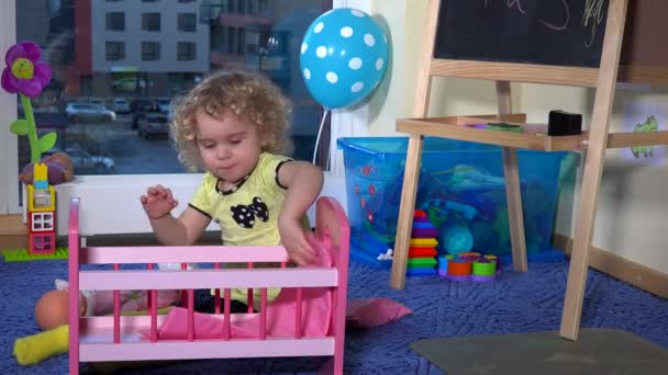Sladká blondýnka batole dívka připravit hračka postel postýlka pro panenku baby doma - Záběry, video
