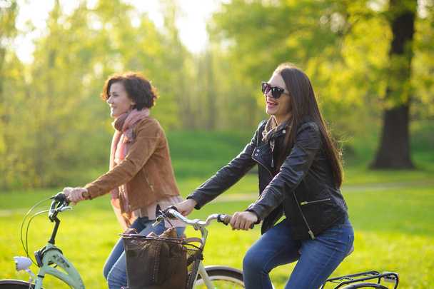 Dwie młode atrakcyjne kobiety jeżdżą na rowerach w parku wiosny. Przyjemność z natury i ruchy. Zdrowy styl życia. - Zdjęcie, obraz
