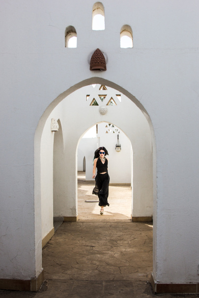 attraktive junge Frau mit Sonnenbrille blickt in die Kamera, während sie an einem weißen Gebäude in Ägypten spaziert     - Foto, Bild