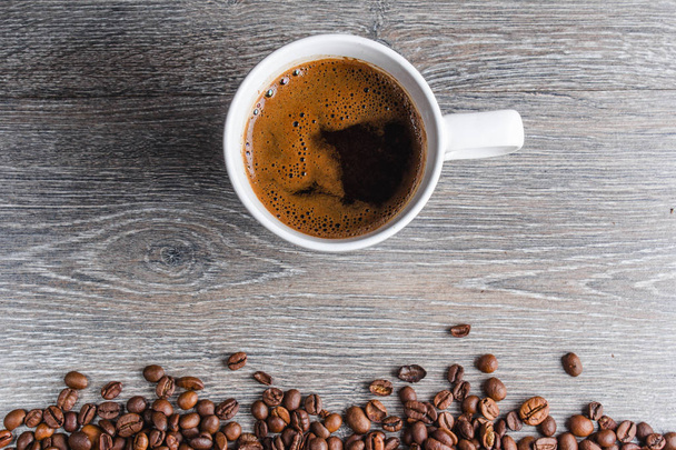 Nahaufnahme einer weißen Tasse Kaffee mit Bohnen auf Holzhintergrund - Foto, Bild