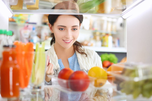 Sağlıklı yiyecek, sebze ve meyvelerle dolu açık buzdolabının yanında duran kadın portresi. Kadın portresi - Fotoğraf, Görsel
