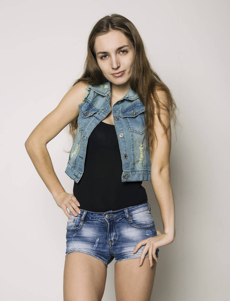 young beautiful happy stylish hipster girl in a denim jacket and shorts posing on a light background - 写真・画像