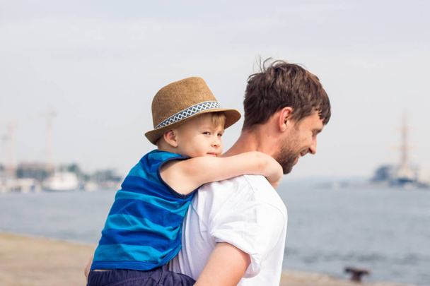 お父さんと息子のビーチで。海。夏。幸せなパパと息子が歩いて、ボートを見て. - 写真・画像