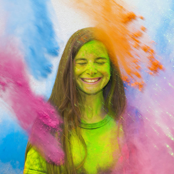 Νέοι χαρούμενο κορίτσι κάτω από την έκρηξη της χρώμα σε σκόνη στο κόμμα Holi χρώματα (χρώματα). Παγώσει κίνηση (stop motion) χρώμα σε σκόνη έκρηξη ή ρίχνουν σκόνη χρώματος. Πολύχρωμα γκλίτερ έκρηξη. - Φωτογραφία, εικόνα