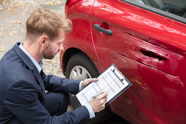 Insurance Agent Writing On Clipboard While Examining Car After Accident - Photo, Image