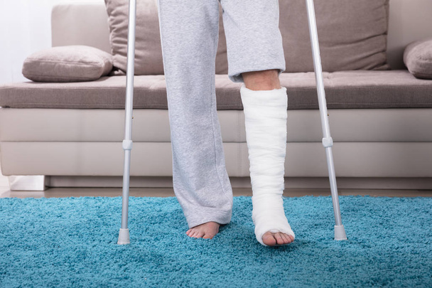 Man With Broken Leg Using Crutches For Walking On Blue Carpet - Fotó, kép