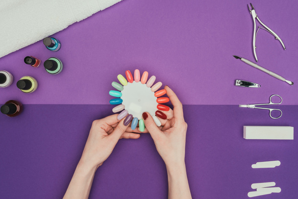 обрезанное изображение женщины, выбирающей цвет для ногтей с палитрой маникюра
 - Фото, изображение