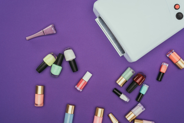 bovenaanzicht van verspreide nagel poetsmiddelen en UV-lamp geïsoleerd op paars - Foto, afbeelding