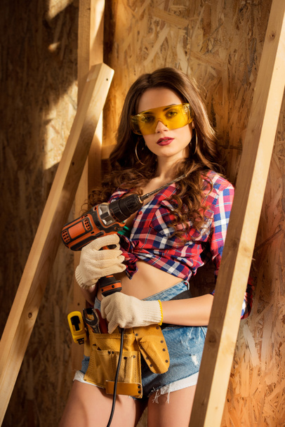 atraente mulher sexy em óculos com broca elétrica posando na construção
 - Foto, Imagem