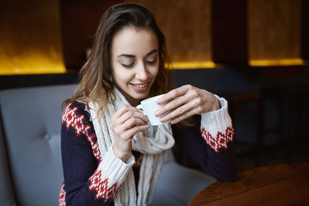 Lachende vrouw gekleed in een trui en sjaal in café met kopje koffie - Foto, afbeelding