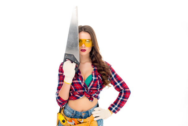 beautiful girl in goggles with tool belt holding saw, isolated on white - Photo, image