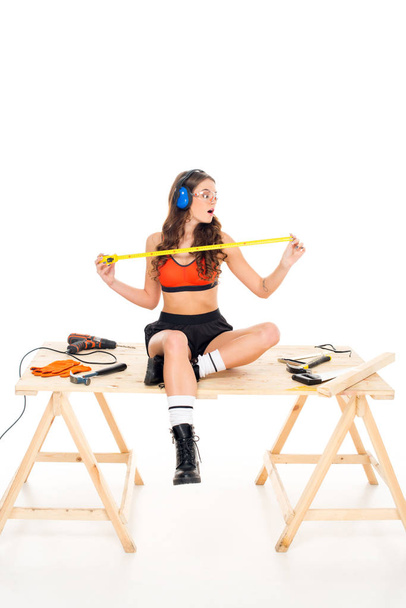 fille séduisante dans des écouteurs de protection assis sur une table en bois avec des outils, isolé sur blanc
 - Photo, image