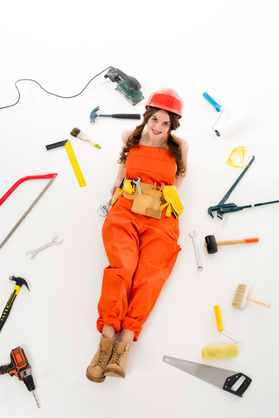 Dziewczyna w kombinezon i kask, leżąc na podłodze z różnych urządzeń i narzędzi, na białym tle, ogólny widok - Zdjęcie, obraz