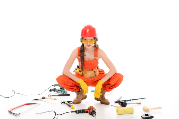 trabajadora confiada en overoles sentada en el suelo con diferentes equipos y herramientas, aislada en blanco
 - Foto, imagen
