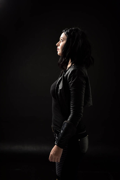 ritratto di ragazza dai capelli neri che indossa abiti in pelle, illuminazione lunatica su sfondo nero
. - Foto, immagini