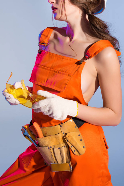 cropped view of girl in overalls with tool belt and goggles, isolated on blue - Foto, Bild