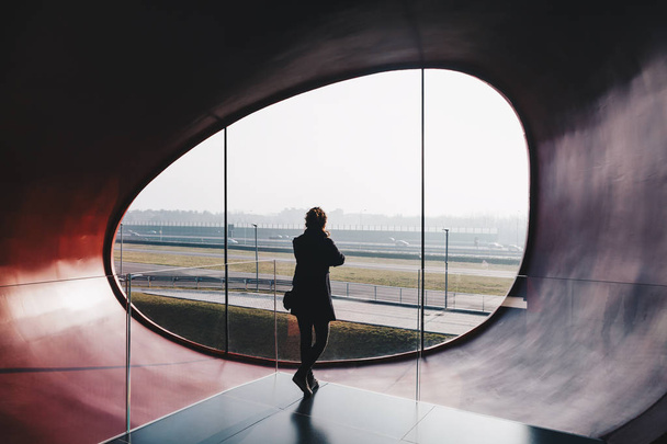 donna in piedi in un edificio per uffici futuristico e moderno, guardando all'esterno finestra ovale moderna
 . - Foto, immagini