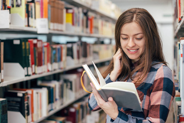 Young female girl  student smiling with book in library - Φωτογραφία, εικόνα