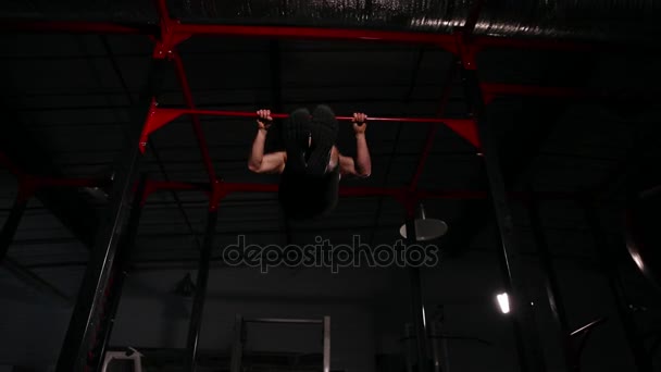 A sportoló fekete ruhában, az edzőteremben egy konnektorba végez a vízszintes sáv. A széles látószögű Nézd alatt. - Felvétel, videó