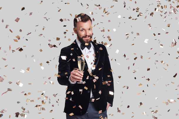 Cheers from Handsome young man in suit holding glass with champagne, confetti falling - Photo, Image